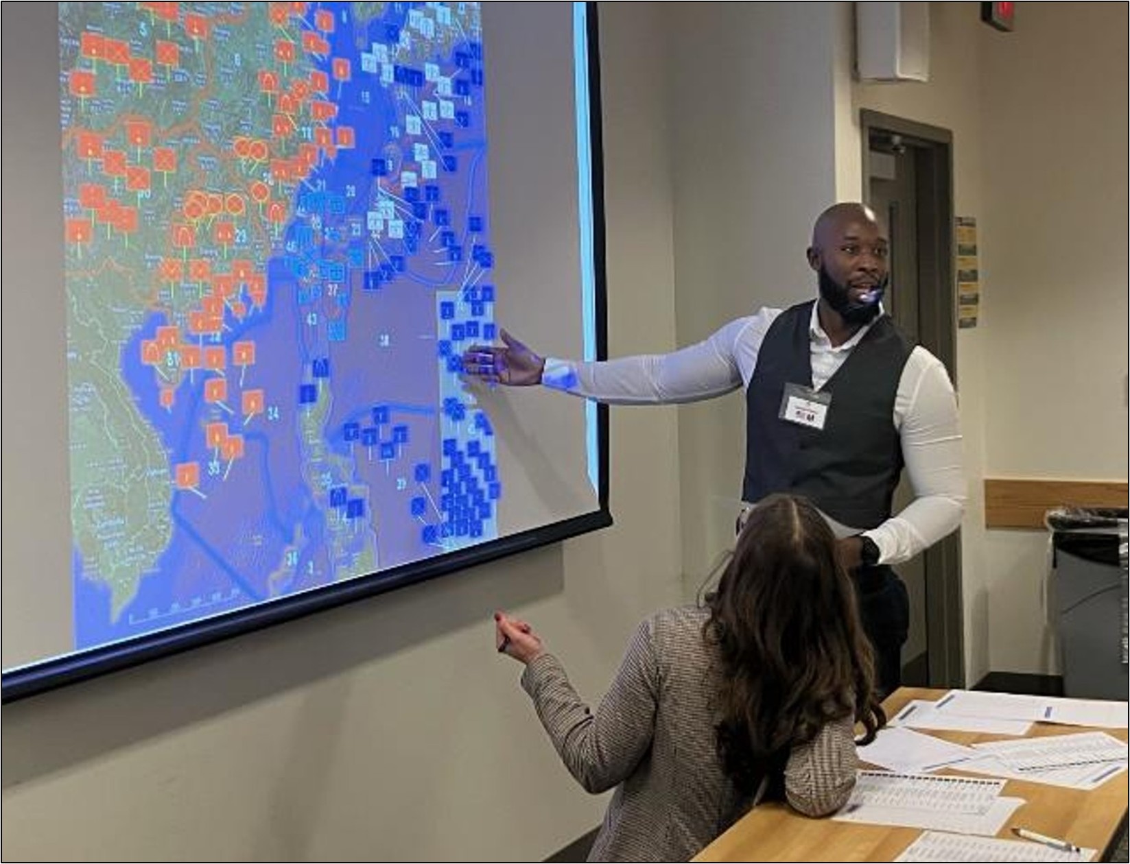 A participant presents simulation results using a projected digital map during a classroom exercise.